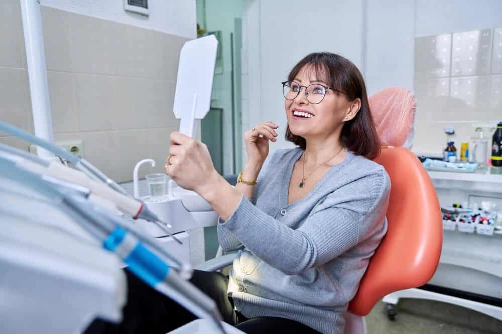 Woman in a dental chair in Cheltenham checking her teeth, illustrating a dental implant consultation